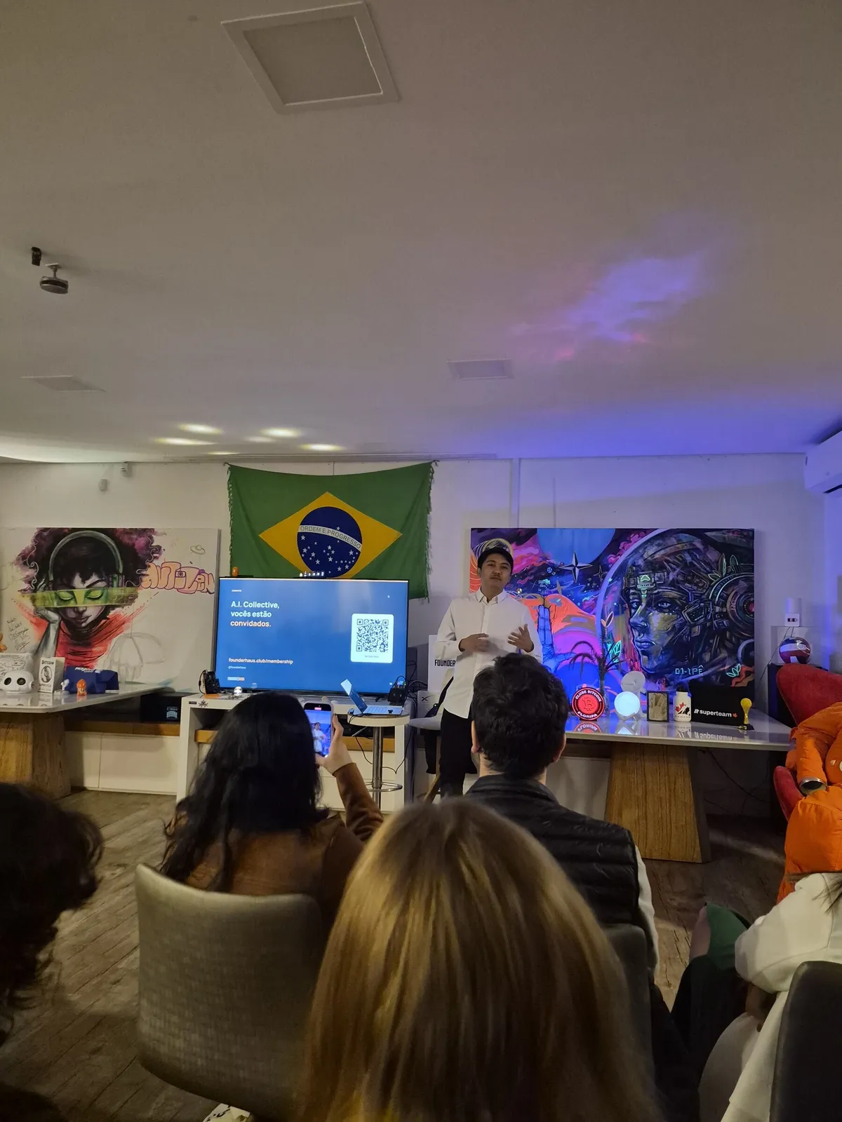 Thiago at the front of the room inviting people to join the community, a QR code on the screen.
